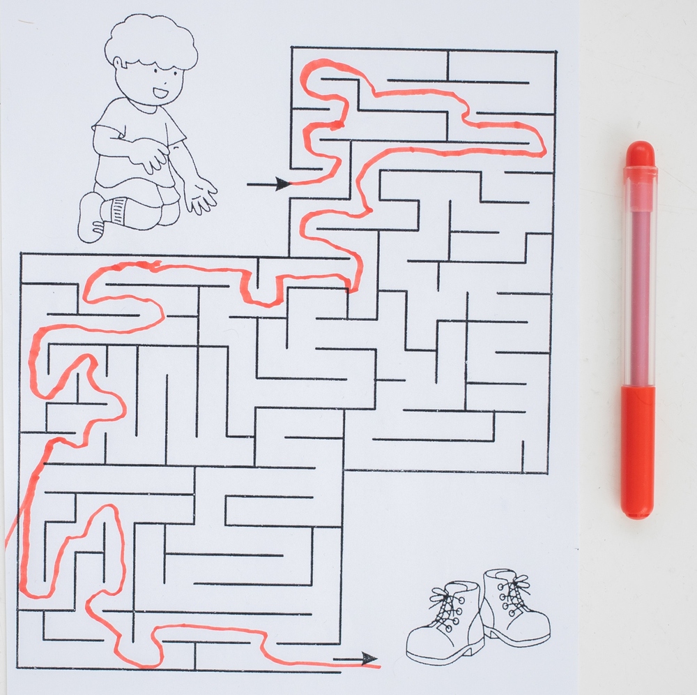 drawing of toddler sitting next to paper maze entrance with red line drawn through correct path to a pair of boots.